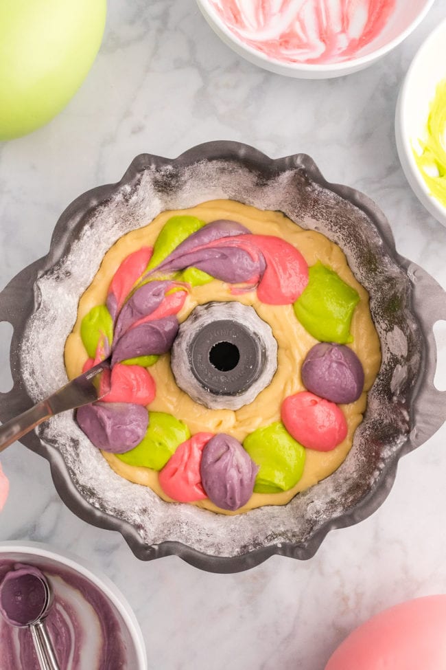 scoops of colorful batter added to cake batter in a bundt pan