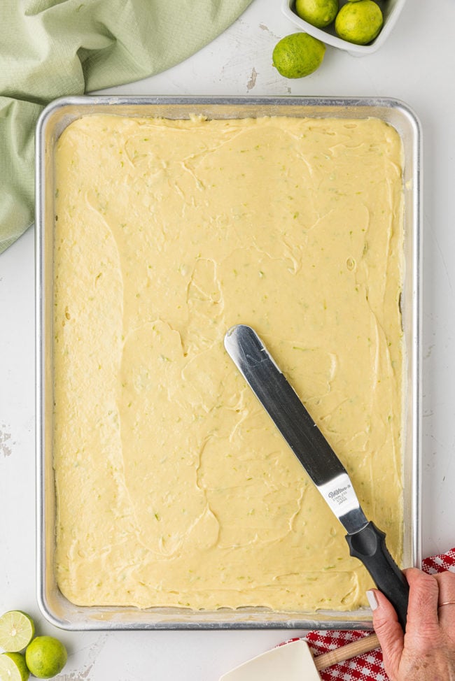 cake batter being spread out in a sheet pan with an offset spatula