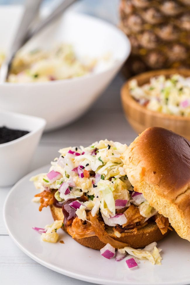 pineapple coleslaw piled on a pulled pork sandwich