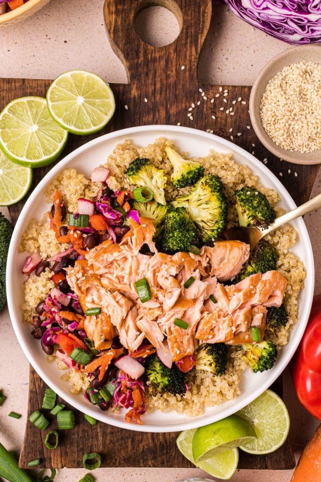 white bowl with salmon, veggies and quinoa and fresh lime.