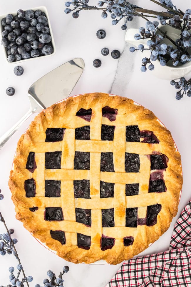 baked pie with lattice pie crust with fresh blueberries next to it.
