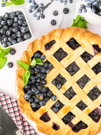 a blueberry pie with fresh blueberries and mint on top of the lattice crust