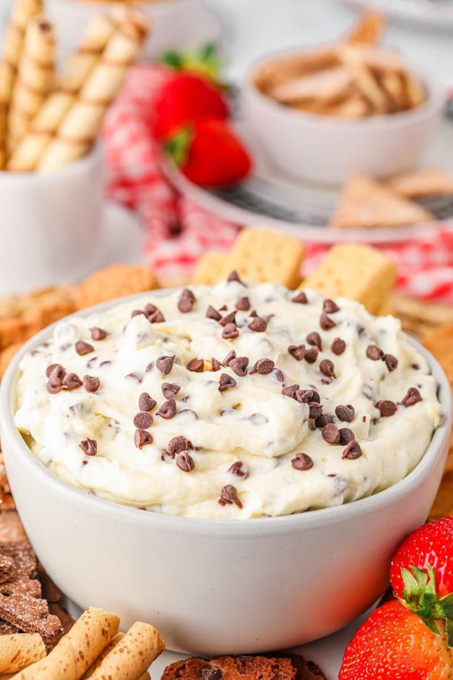 close up of cannoli dip in white bowl with chocolate chips on top and cookies in background