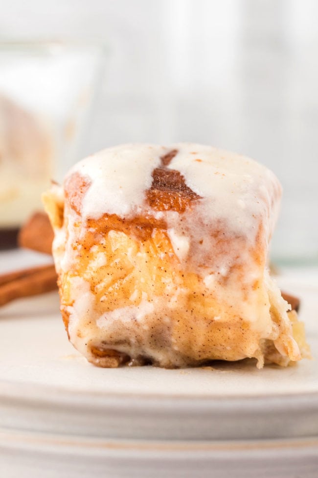 close up of a homemade cinnamon bun on a stack of white plates with a cinnamon stick