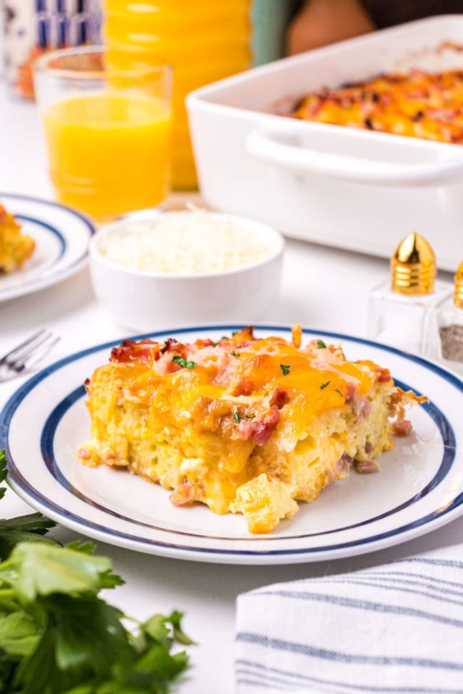 egg casserole on a white plate with a casserole dish and orange juice in the back ground