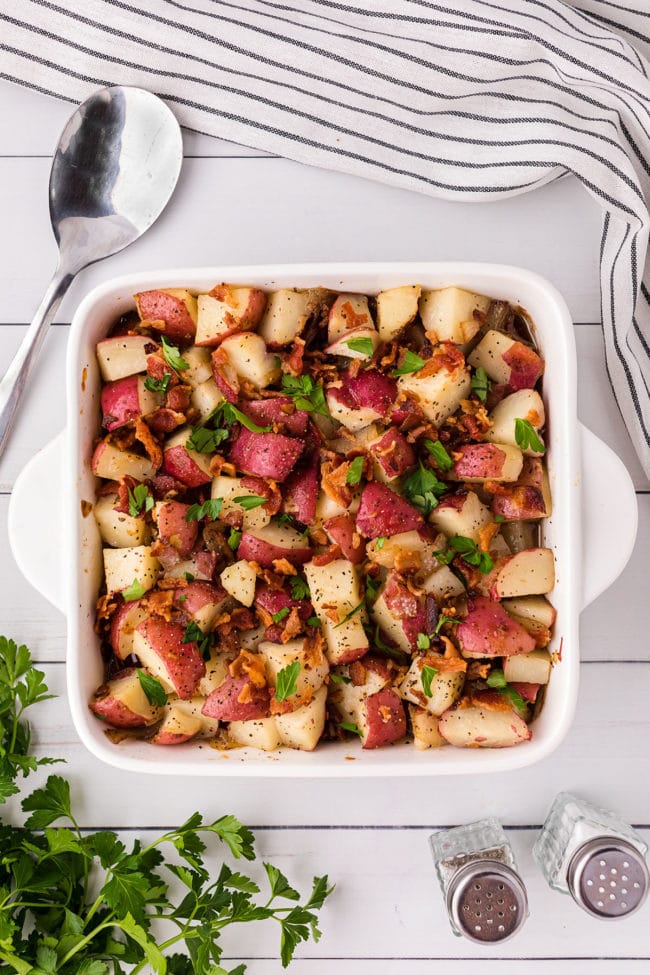 german potato salad in a square white baking dish on a counter with a serving spoon