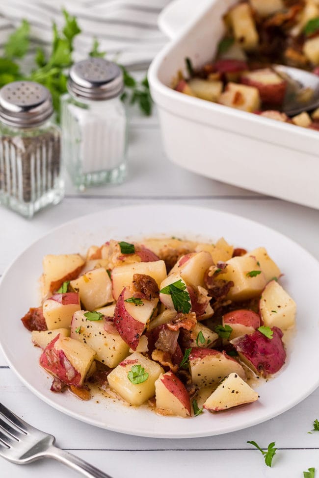 potato salad on a white plate and in a baking dish on a counter with salt and pepper shakers in the background.