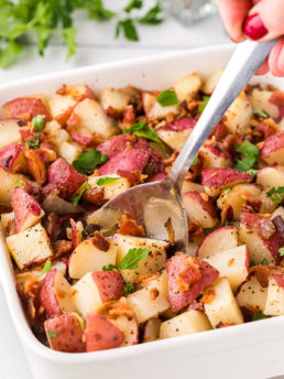 potato salad with red skinned potatoes in a baking dish with a serving spoon