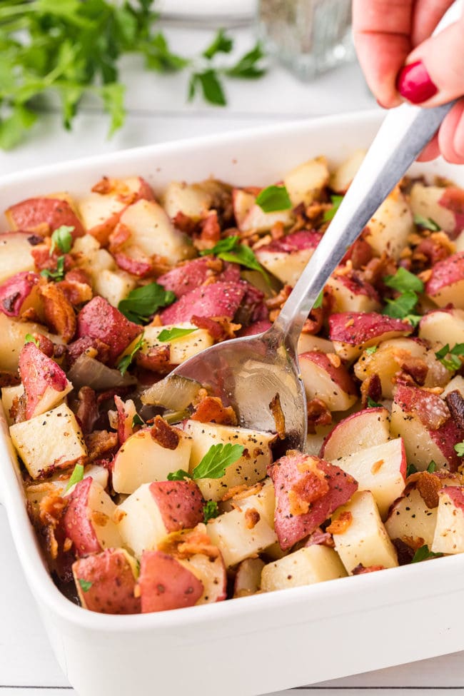 potato salad with red skinned potatoes in a baking dish with a serving spoon