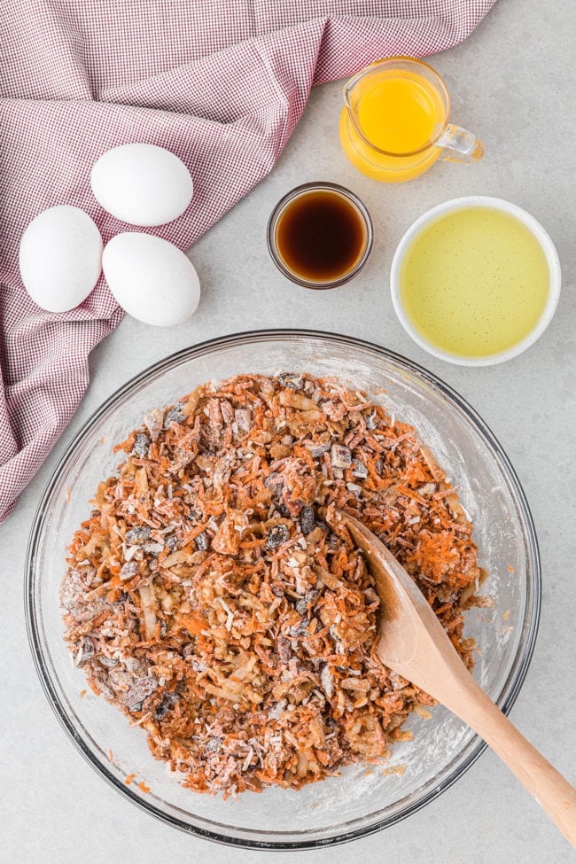 morning glory muffin batter with grated carrots in a glass bowl with a wooden spoon