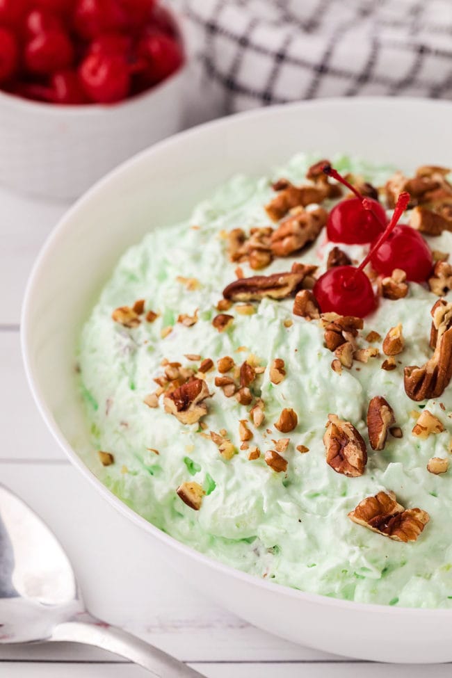 green fluff salad in a white bowl with chopped nuts and cherries on top