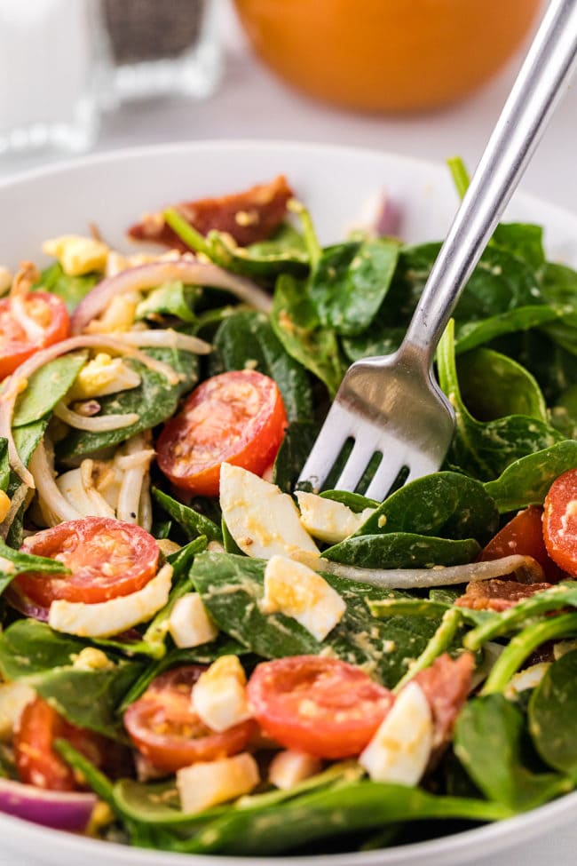 spinach salad in a white bowl with a fork