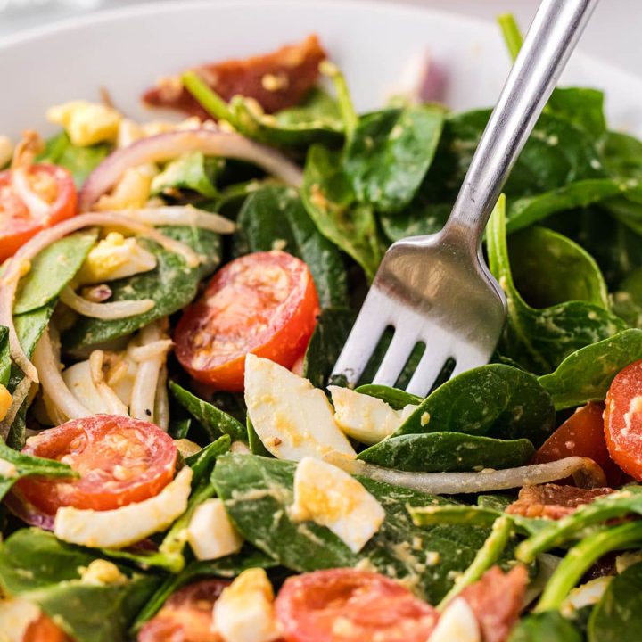 spinach salad in a white bowl with a fork