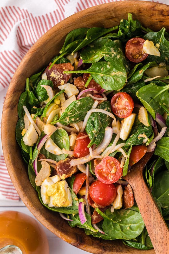 spinach salad with bacon and hard-boiled eggs in wood bowl