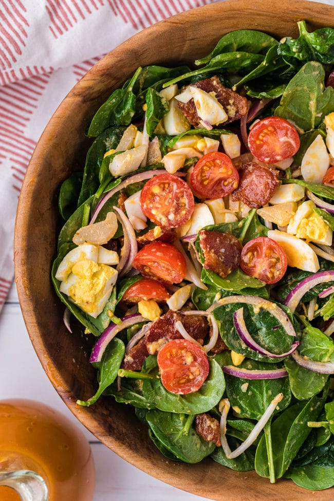 salad in a wood bowl with a red and white towel and bottle of dressing