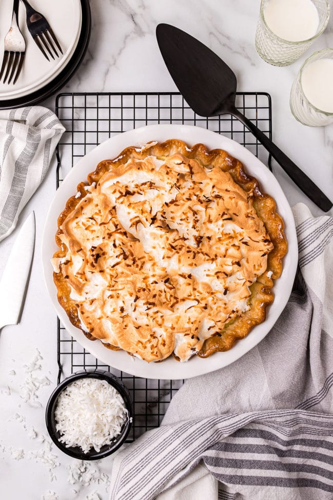 Fresh baked coconut pie on a cooling rack with a pie server