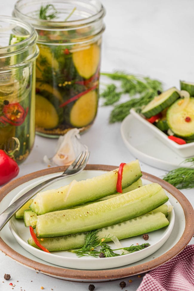 pickle spears on a plate with jars of pickles in the background