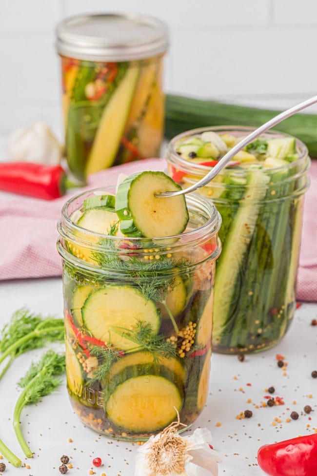 a widemouth canning jar with refrigerator pickles and fresh dill and a fork removing a pickles from the jar.