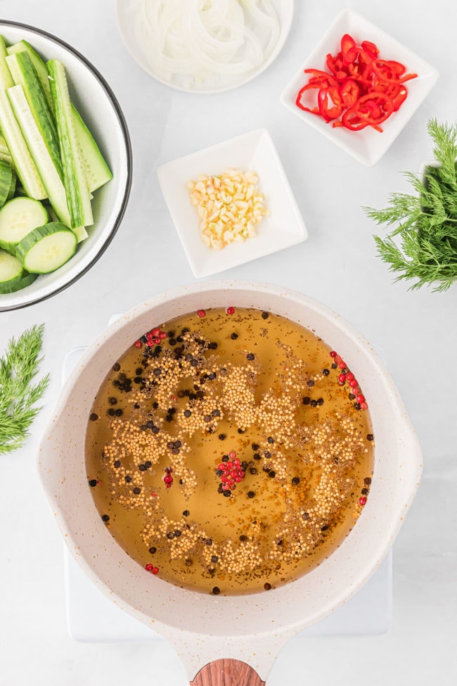 pickle brine in a white pot with cut up vegetables around it