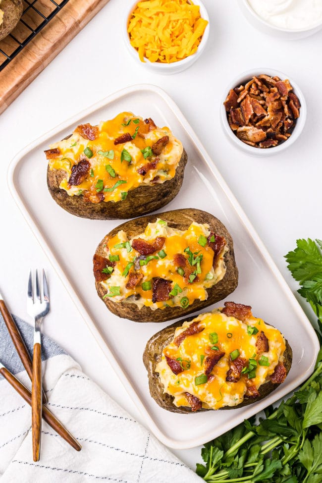 white tray with cheesy stuffed potatoes on a white tray with forks on the side.