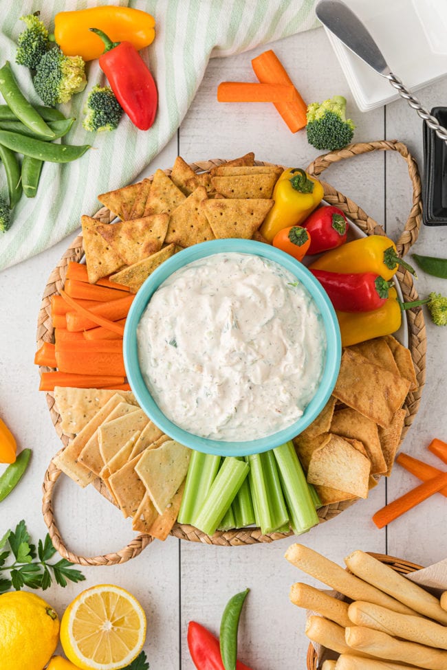 a round tray with crab dip in a bowl surrounded by veggies and crackers