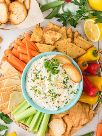 a round tray with crab dip in a blue bowl surrounded by veggies and crackers