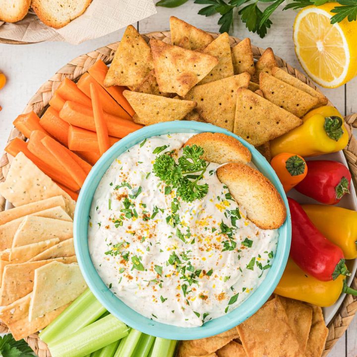 a round tray with crab dip in a blue bowl surrounded by veggies and crackers