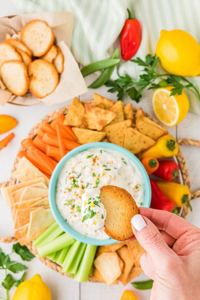 crab dip platter with a woman's hand over the bowl with a cracker dipped.