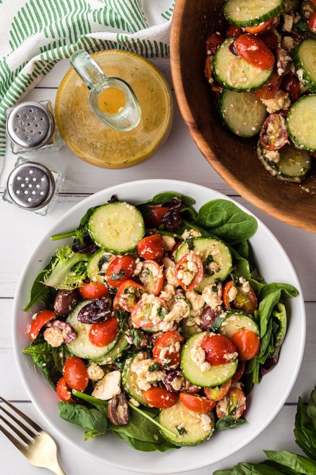 tomato cucumber feta salad plated and in a wooden bowl and dressing in a cruet