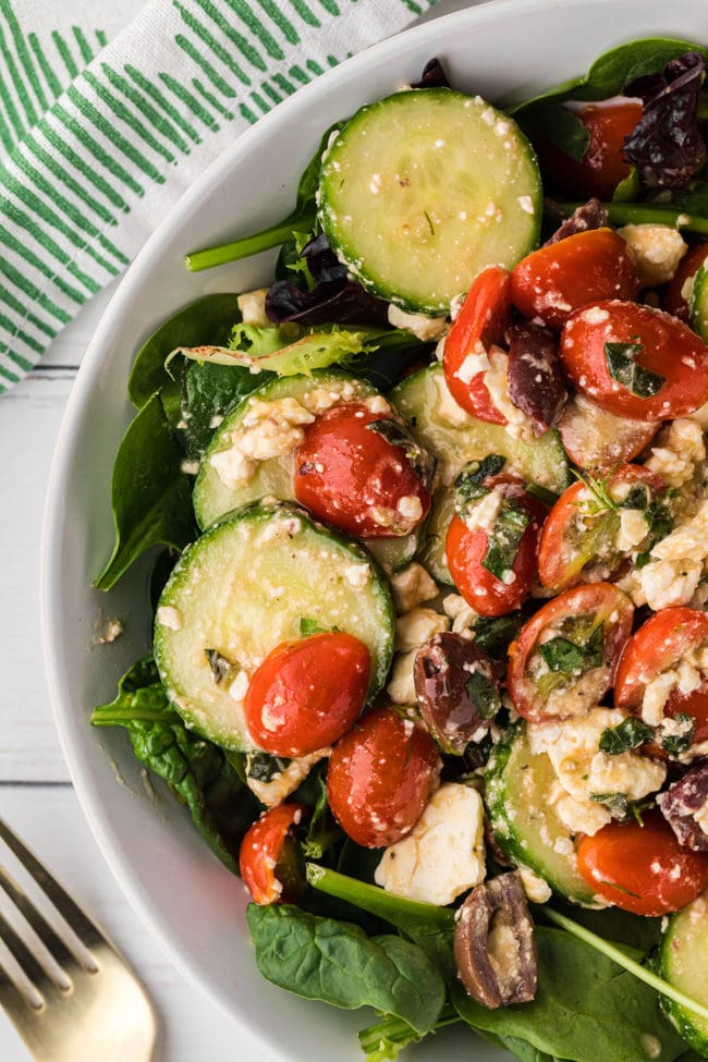 tomato cucumber salad in a bed of greens in a white bowl with a green and white napkin