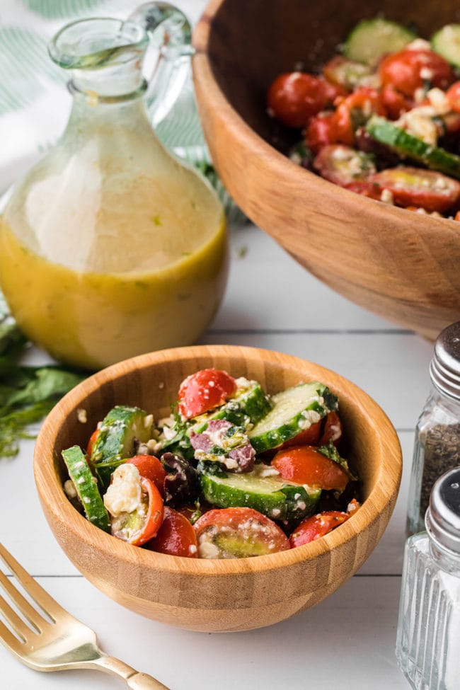 wooden bowls with tomato cucumber feta salad and homemade dressing in a cruet