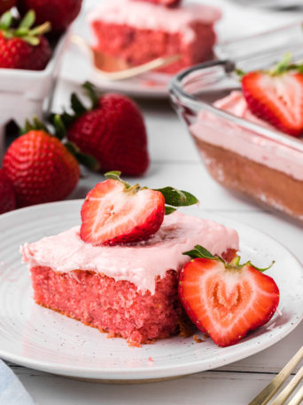 a slice of strawberry cake with butter cream frosting and fresh strawberries