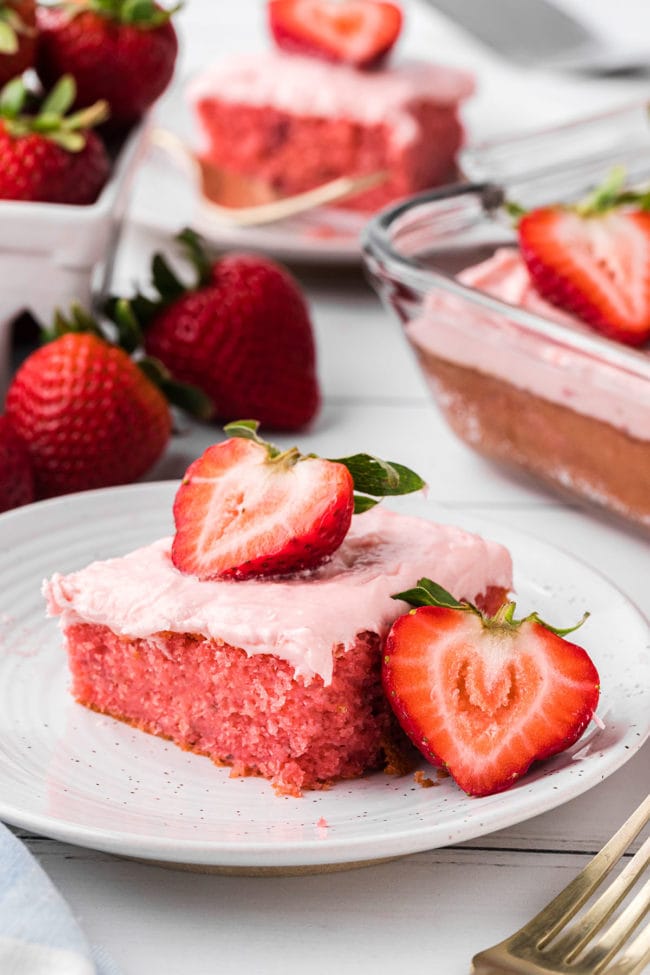 a slice of strawberry cake with butter cream frosting and fresh strawberries