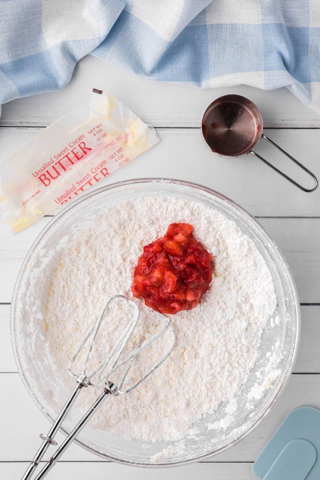 adding fresh strawberries to homemade butter cream frosting in a mixing bowl with beaters