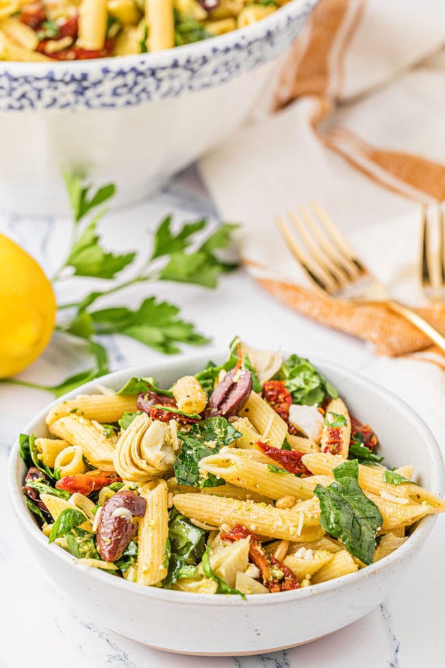 A small bowl of pasta salad with a large serving bowl in the background