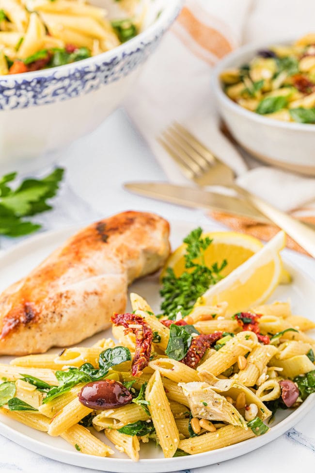 A dinner plate with chicken and Greek pasta salad and fresh lemon wedges.