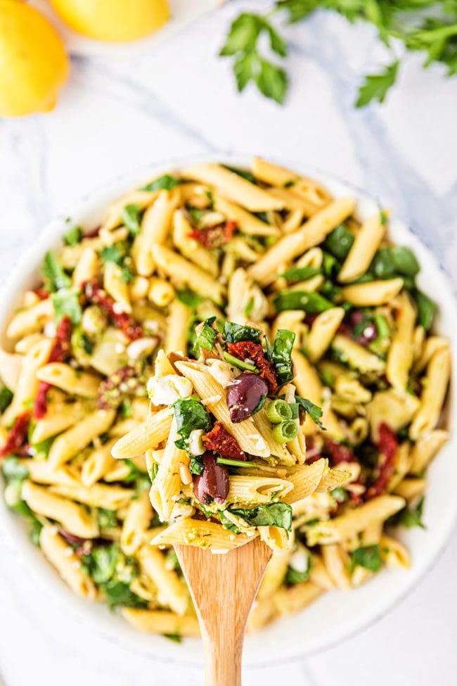 wooden spoon with pasta salad over a bowl of the Greek salad.