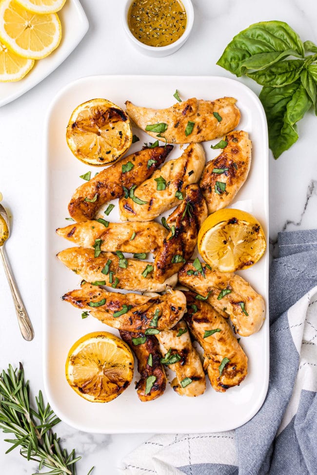 grilled lemon chicken on a white platter with fresh basil