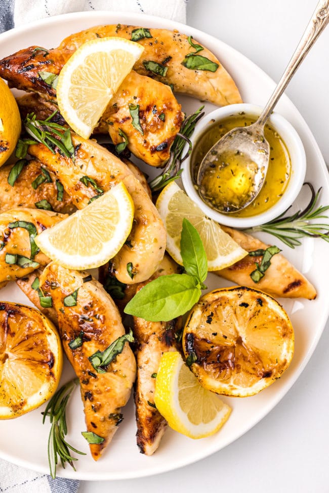 grilled chicken with lemons, fresh rosemary and basil on a plate.