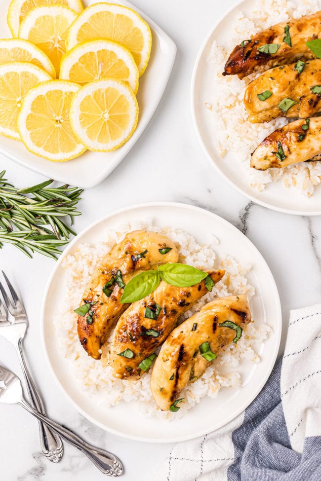 grilled chicken tenders over white rice on a plate with fresh lemons and rosemary in the background