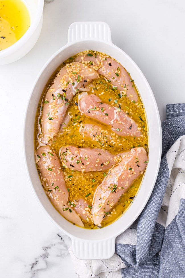 raw chicken tenders in a bowl with lemon garlic and fresh herb marinade