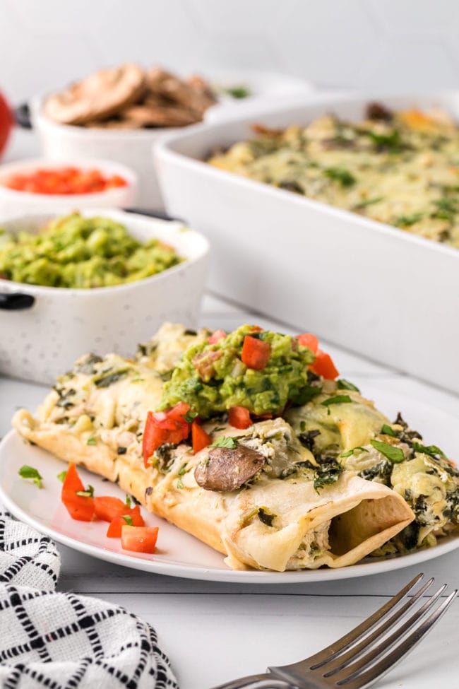 homemade chicken enchiladas casserole with creamy white sauce on a plate next to a casserole dish