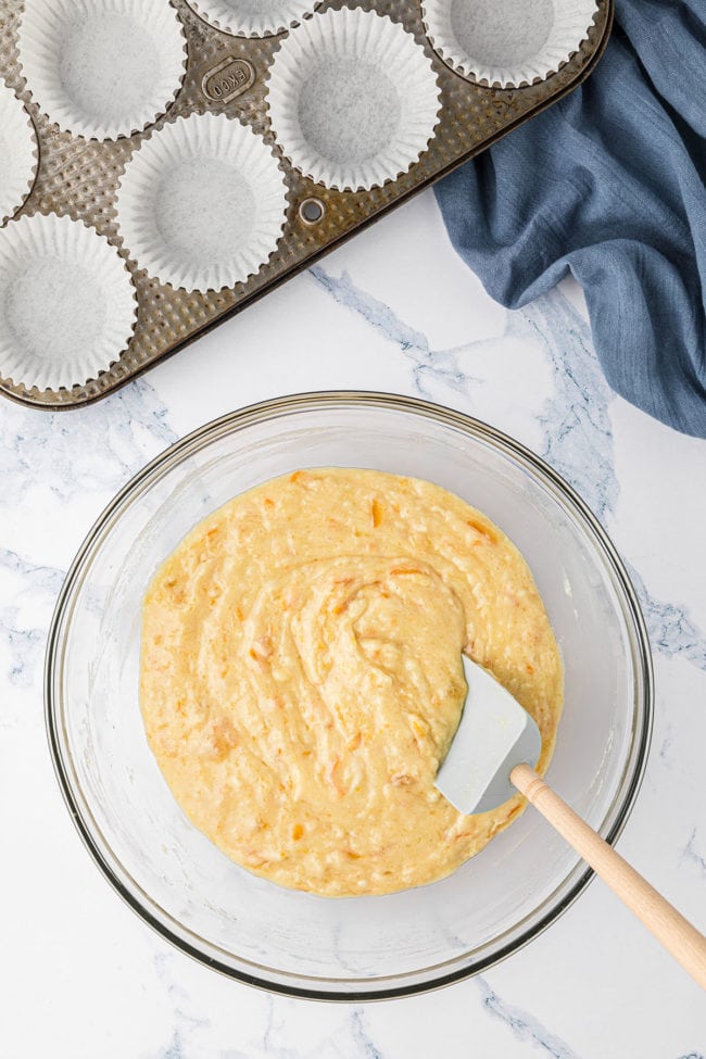 Orange Muffin batter in a glass mixing bowl with a rubber spatula