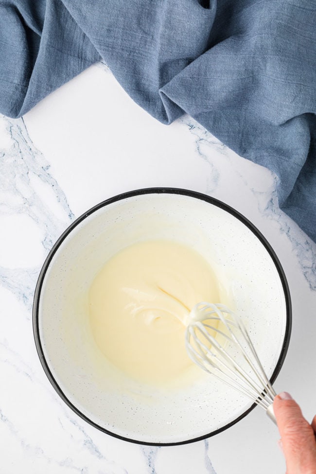 glaze for muffins in a bowl with a wire whisk and a blue towel in background