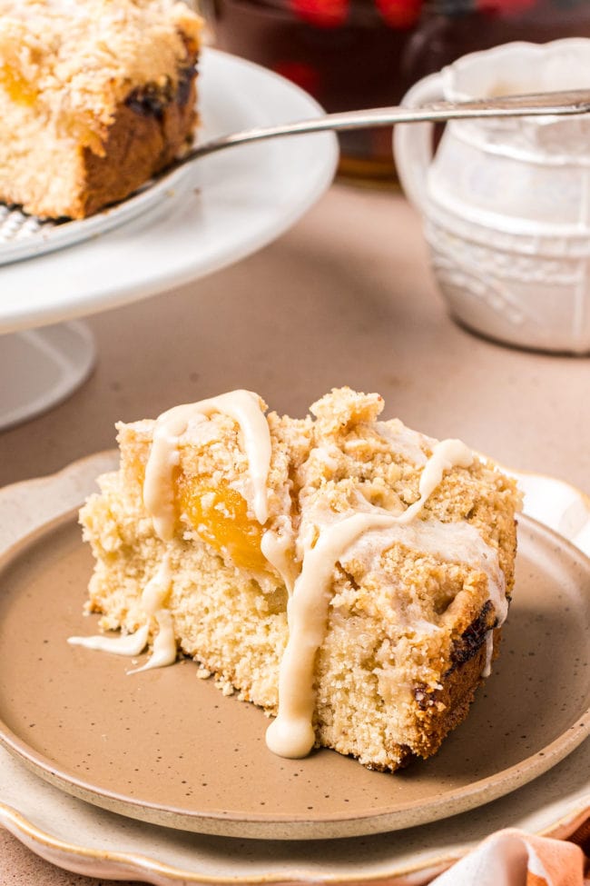 Slice of peach coffee cake on a plate with icing and peaches