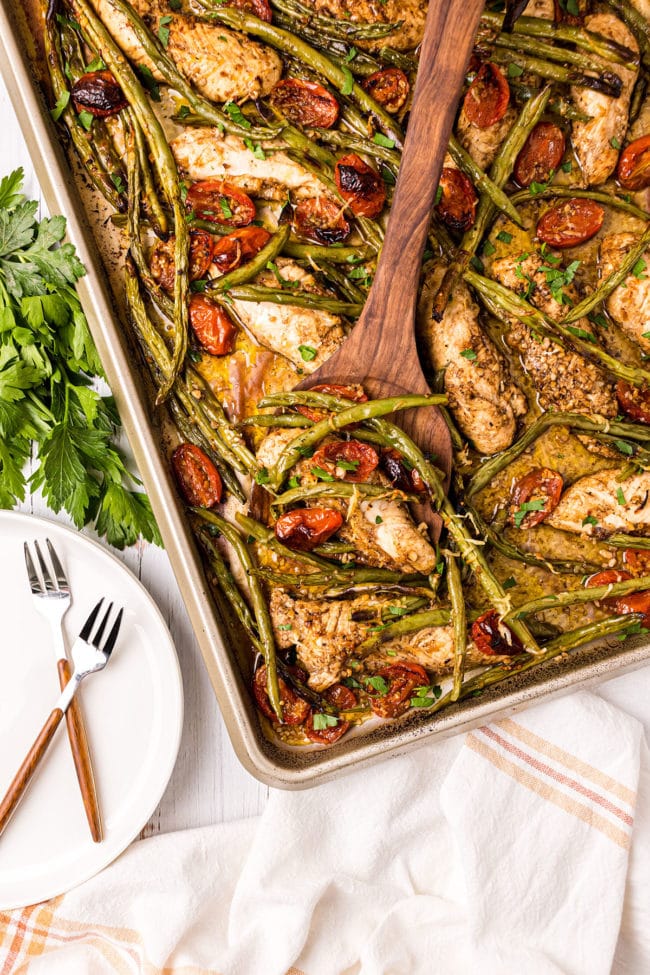 chicken dinner with fresh veggies on a sheet pan with a wooden spatula