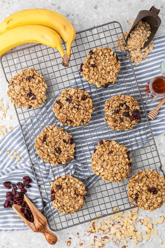 baked breakfast cookies on a cooling rack with bananas, dried cranberries and oats around it.