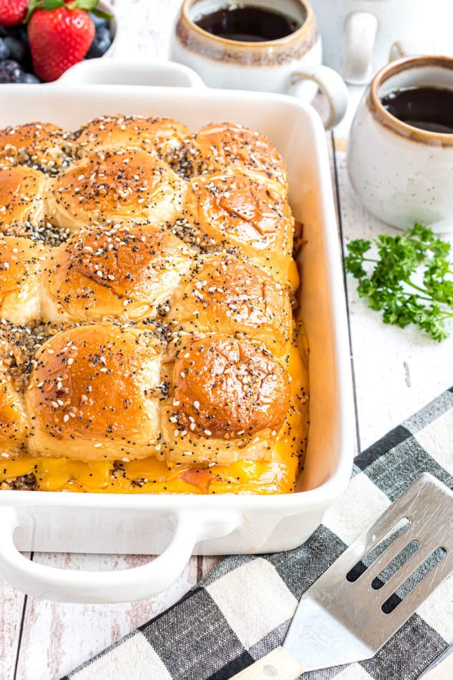 breakfast sliders in a white casserole dish and cups of coffee and fruit in the background