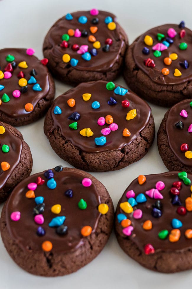 a plate of brownie cookies with rainbow sprinkles on fudgy frosting