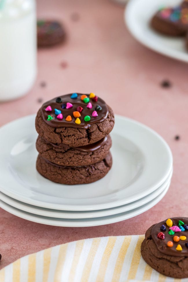 a plate of brownie cookies with rainbow sprinkles on white plates and a pink background